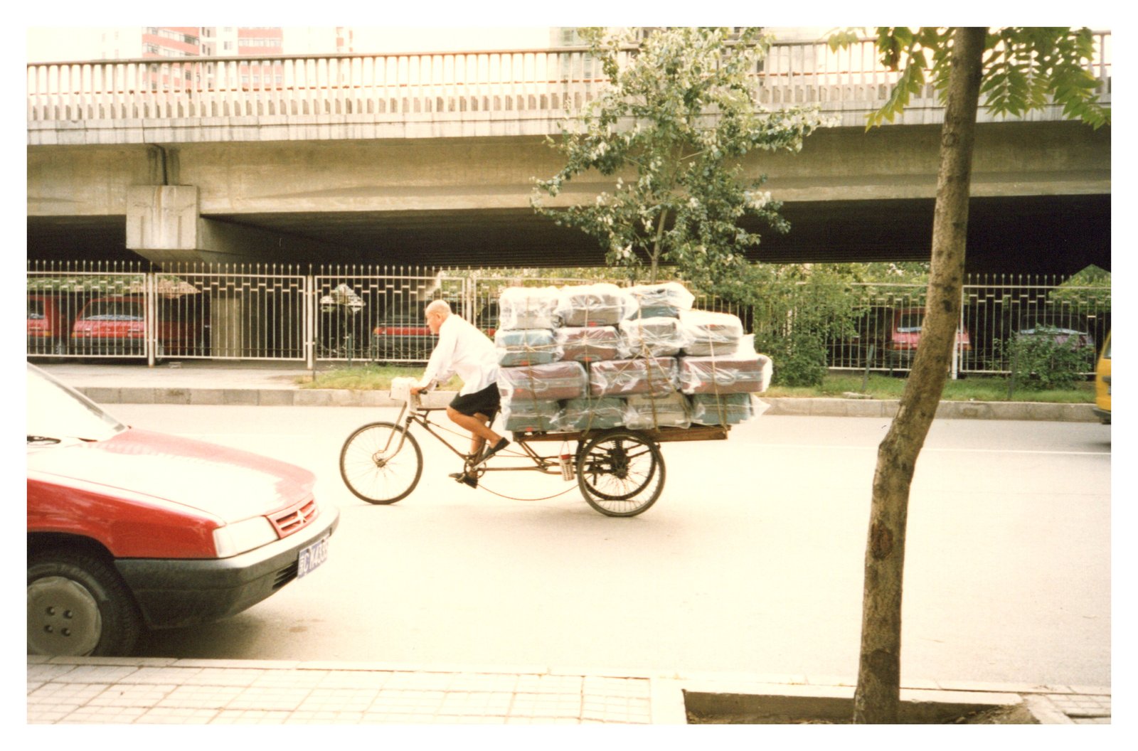 A man on an old bicycle laden with packages, beneath a Beijing overpass